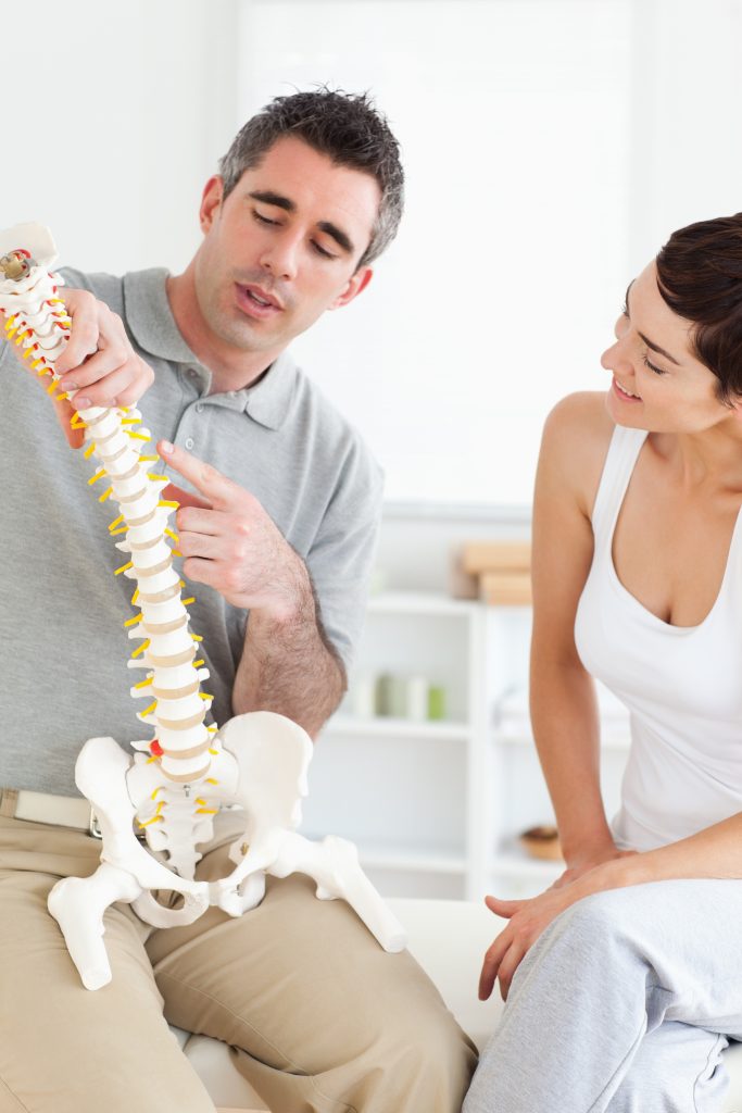 Chiropractor explaining the spine to a woman Urgent care chiropractor explaining a spine model to patient